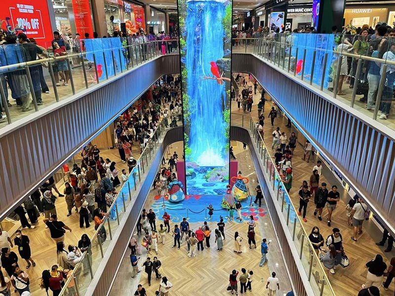Shoppers crowd the atrium as the scenic elevator LED curtain — spanning 3.5 metres wide and 22 metres tall — transforms every ride into an immersive visual journey.